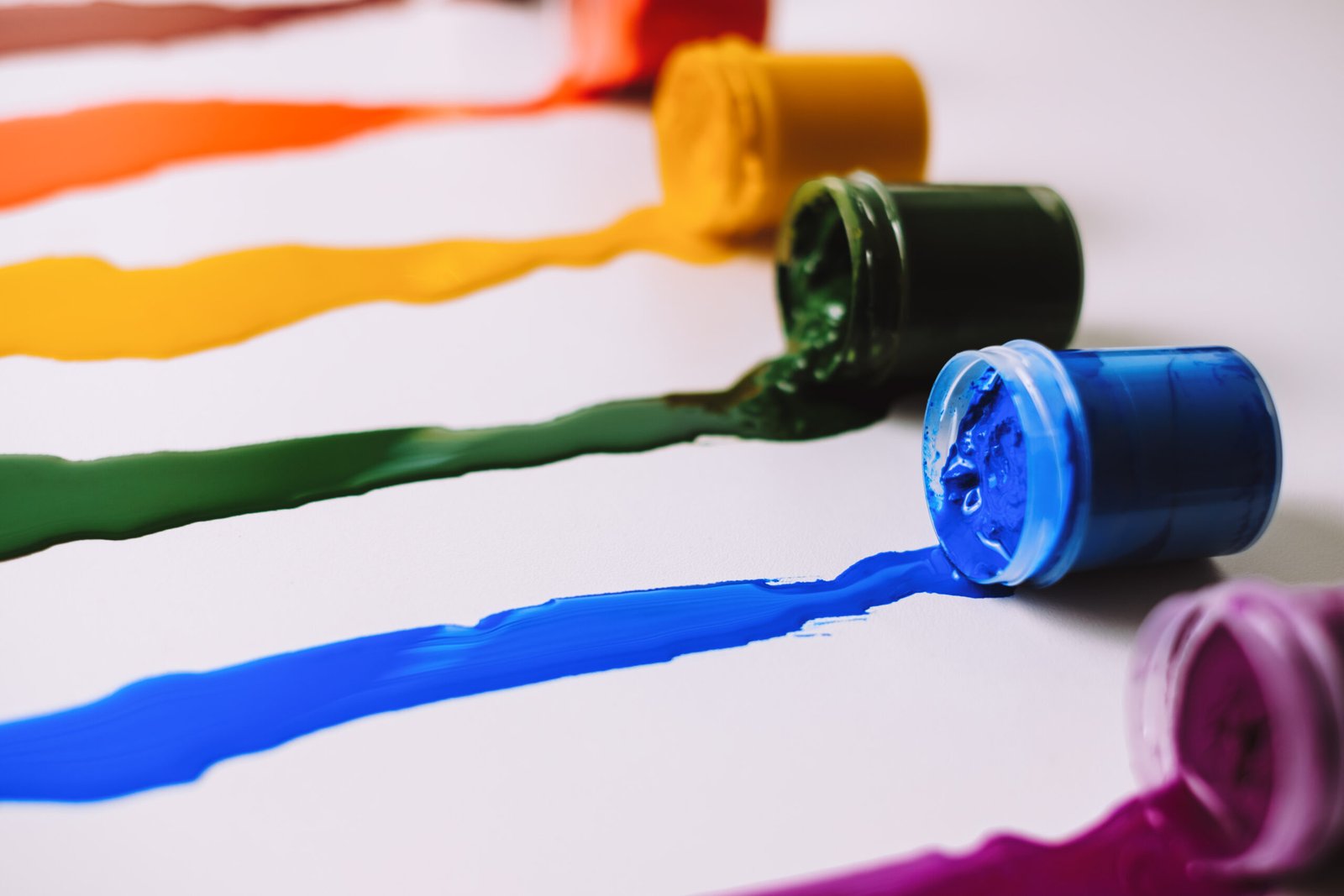 Cans with spilled paint of different colors on a white table.